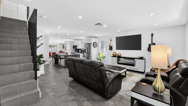 Una sala de estar moderna con un sofá, una mesa de centro y un televisor. Se observa una cocina al fondo con una zona de comedor.