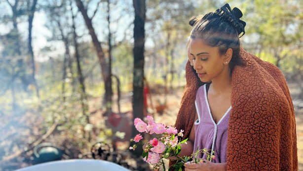 A person holding pink flowers near a bathtub filled with water and flower petals.