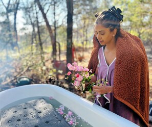 A person holding pink flowers near a bathtub filled with water and flower petals. - Cozy Cabin Retreat in the Woods (Edwardsville)