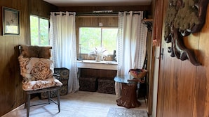 A cozy room with a wooden interior, a cushioned chair, a small table, and a window with curtains.