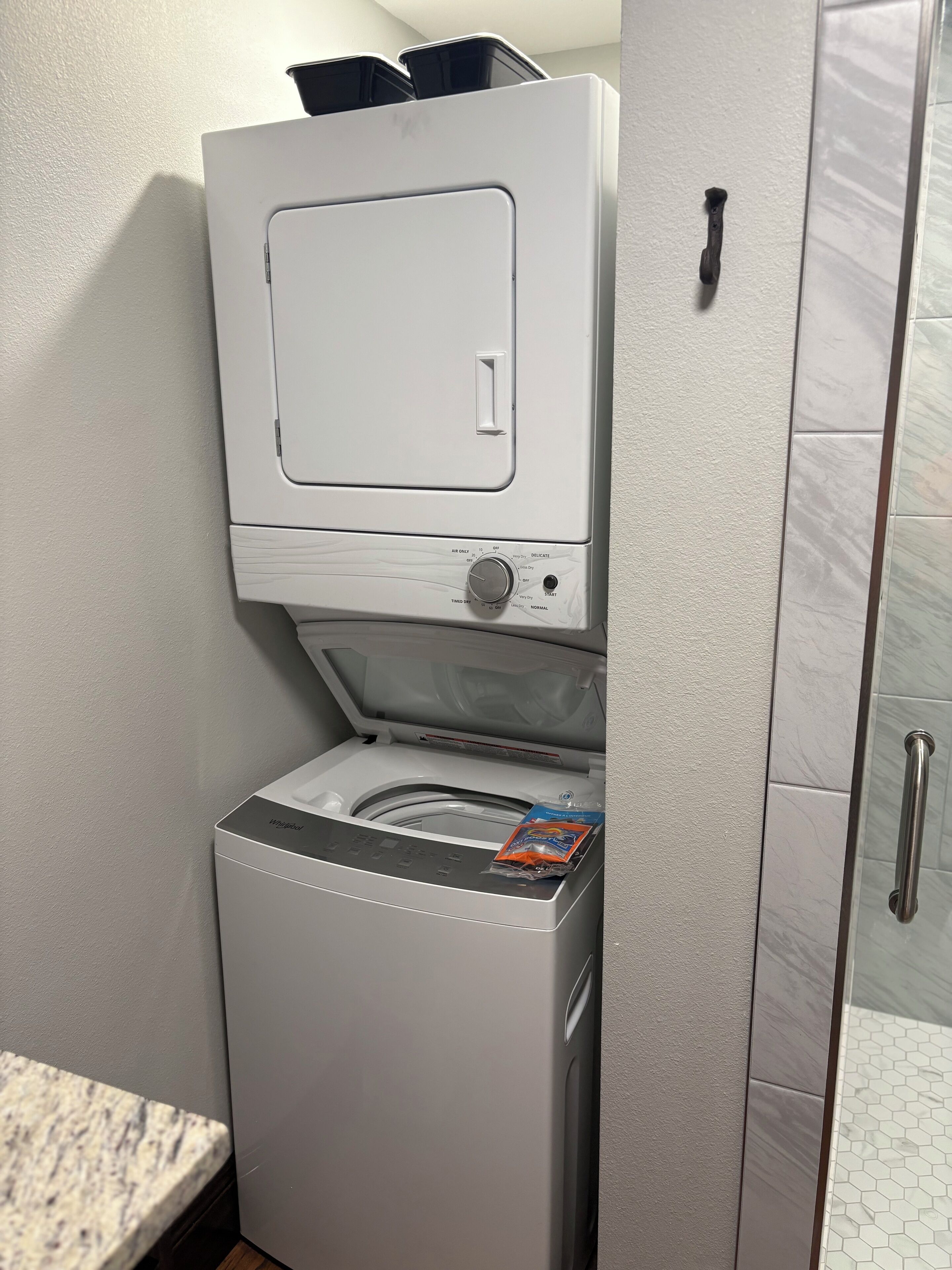 Máquina de lavar compacta, branca e de abertura frontal, com painel de controle e um pequeno pacote de detergente em cima.