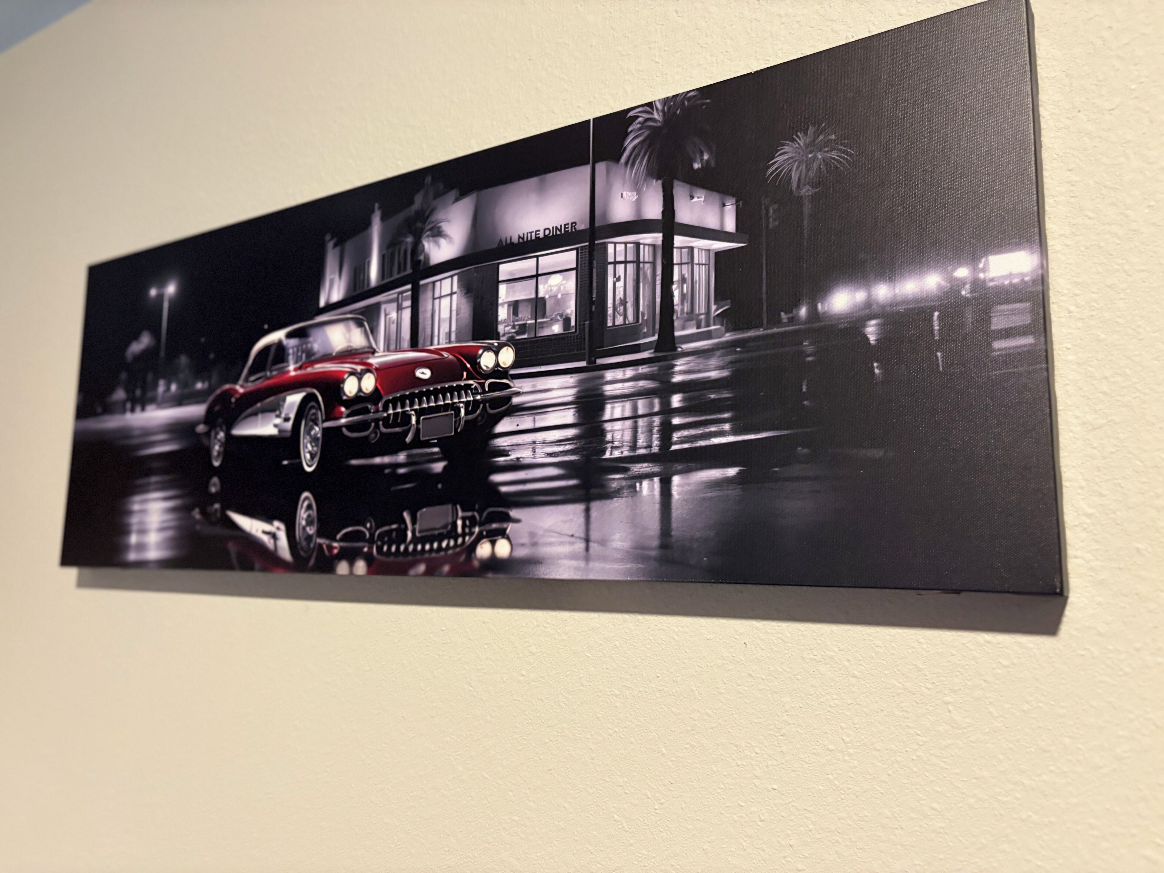 A wall-mounted artwork of a vintage car in front of a building with palm trees.
