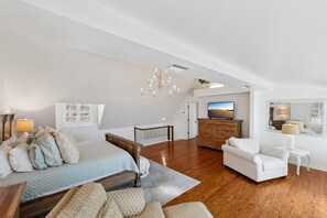 Une chambre spacieuse avec un grand lit, une commode en bois, un fauteuil blanc et un téléviseur.