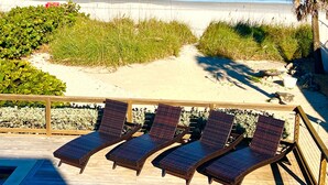 Eine Strandterrasse mit Liegestühlen, ein Sandweg und Blick aufs Meer.