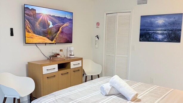 Ein Hotelzimmer mit einem Bett, einem Schreibtisch mit Stuhl, einem Fernseher, einem Deckenventilator und Kunstwerken an den Wänden.