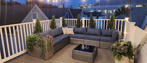 Eine Dachterrasse mit einer Eckcouch, einem Couchtisch und Lichterketten.
