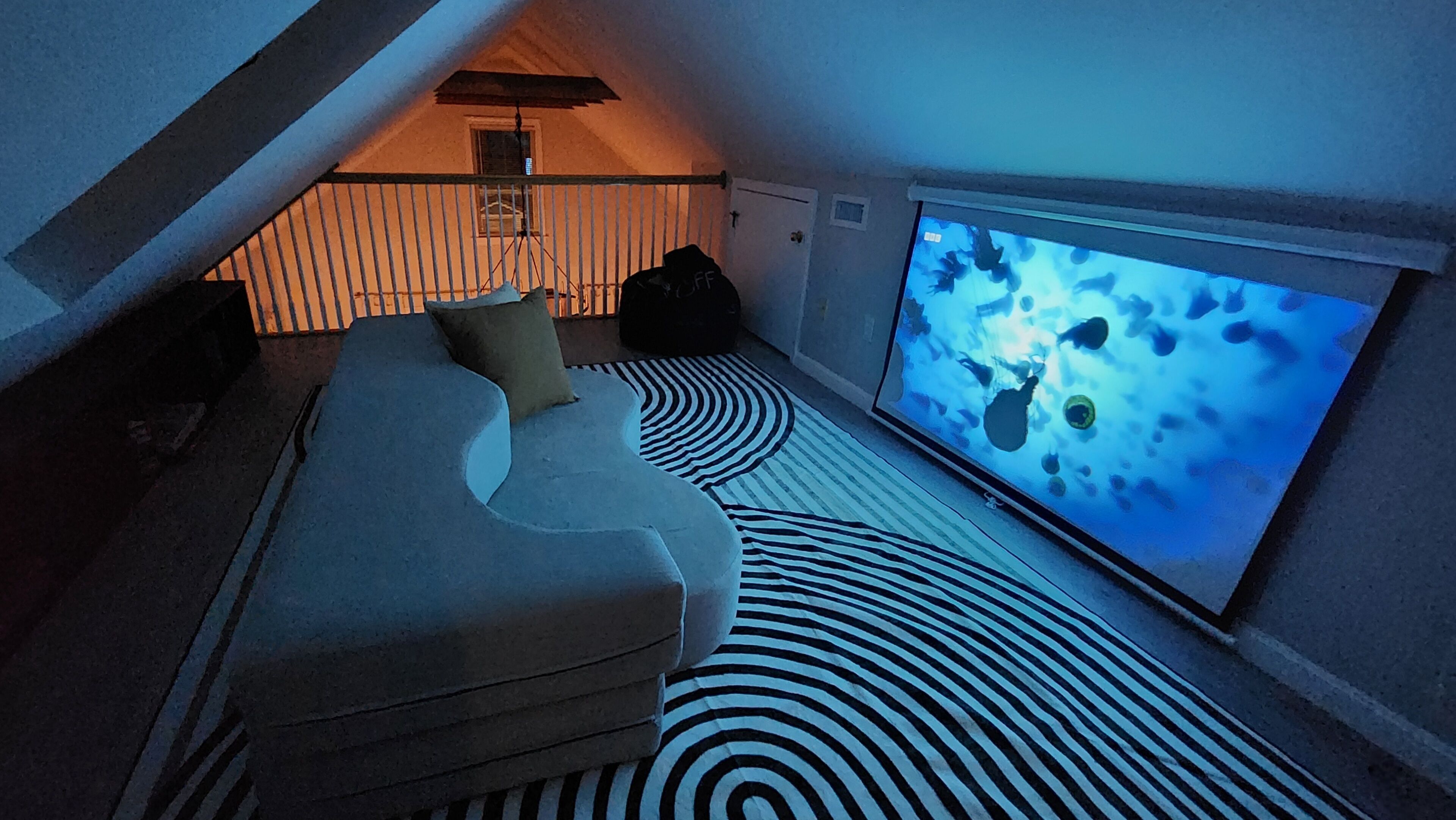 Ein modernes Zimmer mit einer gebogenen Couch, einem gemusterten Teppich und einem großen Bildschirm, der eine Unterwasserwelt zeigt.