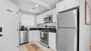 A modern kitchen with white cabinetry, stainless steel appliances, and a patterned rug.