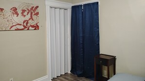 Ein Schlafzimmer mit Holzboden, einem Bett, einem Nachttisch, einem Fenster mit blauen Vorhängen und einer Wand mit einem Blumenbild.