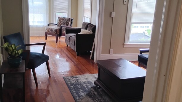 Ein geräumiges Wohnzimmer mit Holzböden, einem dunklen Sofa, einem gemusterten Sessel und einem Couchtisch.