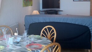 Una habitación con cama, televisión, una mesa con sillas y obras de arte en las paredes.