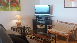 Una sala de estar con un sofá, una mesa de centro, un televisor sobre un mueble, una lámpara y un sillón.