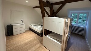 Une chambre avec un lit superposé, une commode, une fenêtre donnant sur un espace verdoyant et un radiateur.