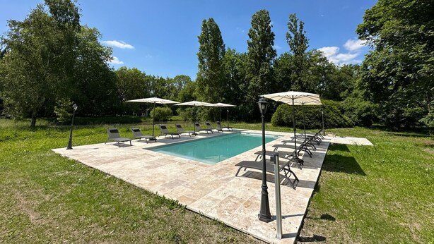 Une piscine rectangulaire, bordée d’une terrasse carrelée, entourée de chaises longues et de parasols.