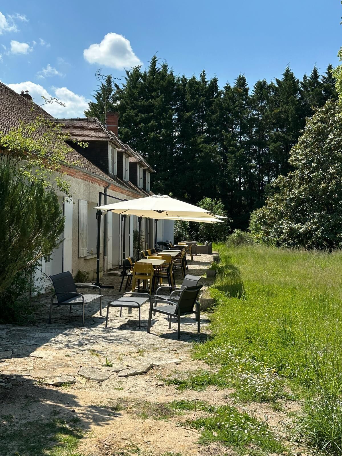 Un patio esterno con tavoli e sedie, una zona coperta con ombrellone e un edificio con tetto in tegole.