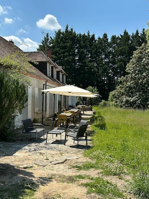 An outdoor patio with tables and chairs, a covered area with an umbrella, and a building with a tiled roof. - Domaine du Patineau (Chevillon-sur-Huillard)