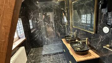 Un baño moderno con paredes de mármol negro, un tocador de madera y un espejo grande.