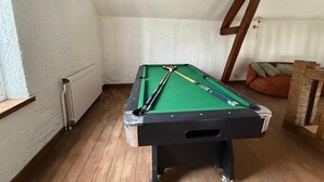 Une table de billard dans une pièce avec des poutres en bois, un radiateur et un coin salon avec des sièges rembourrés.