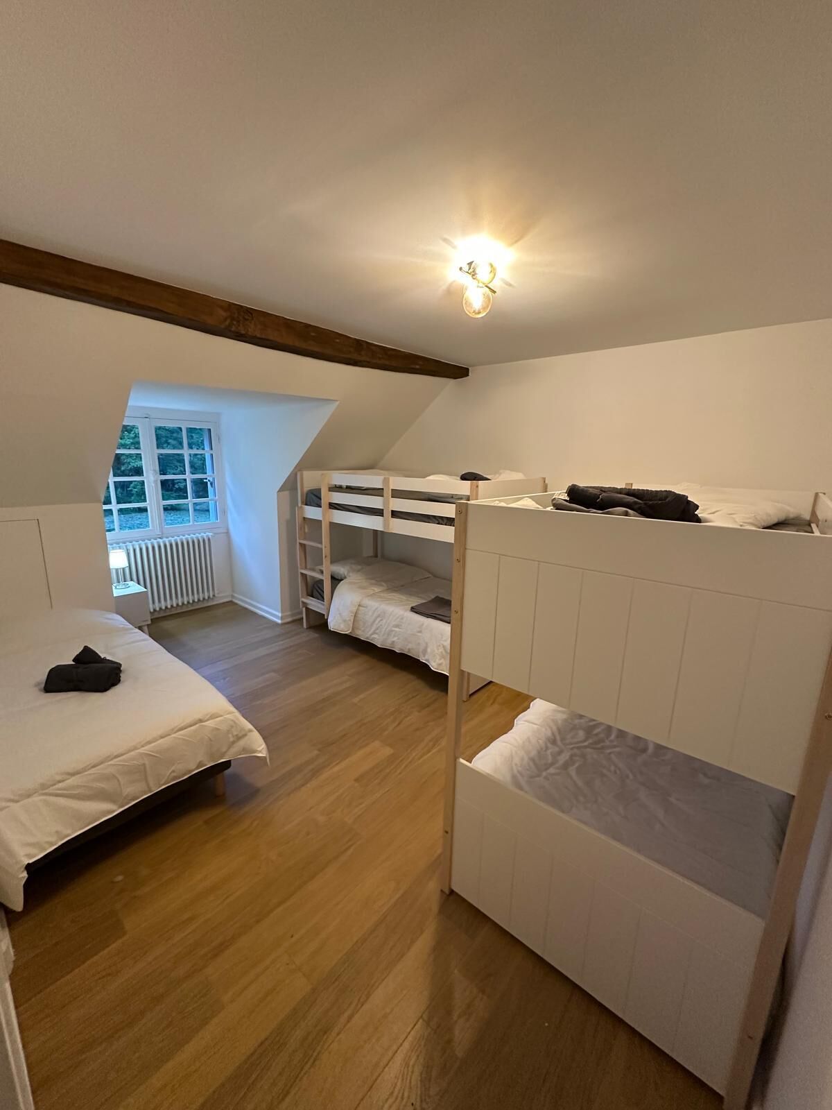 Un dormitorio con literas, suelo de madera, ventana con vistas y una lámpara en el techo.