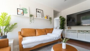 Een moderne woonkamer met een bruine leren bank, een witte salontafel en een flatscreen televisie op een witte kast.