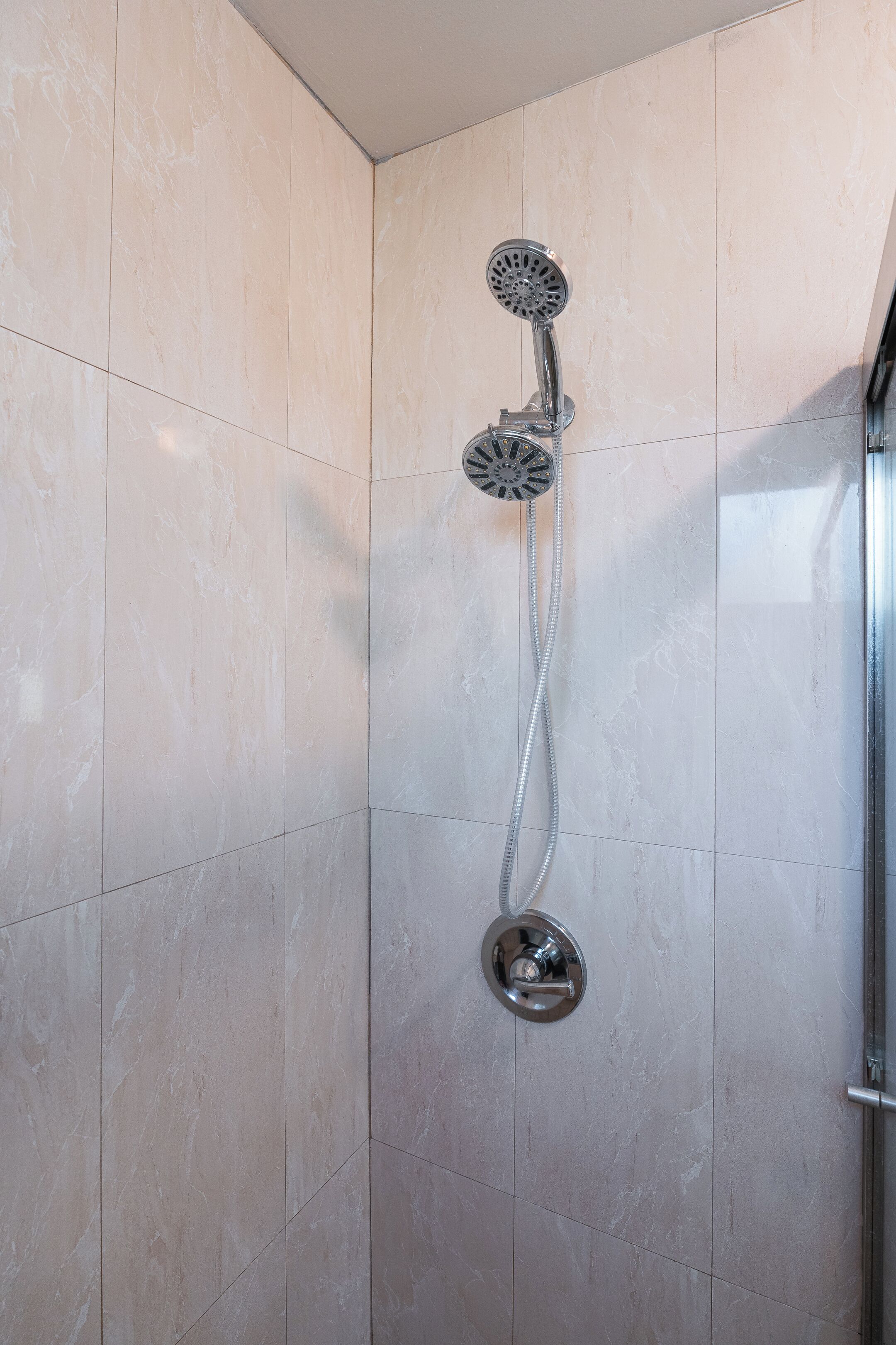 A shower with a handheld showerhead and a fixed wall-mounted showerhead in a tiled bathroom.
