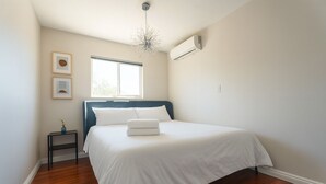Een slaapkamer met een bed, nachtkastje, raam en airconditioning.