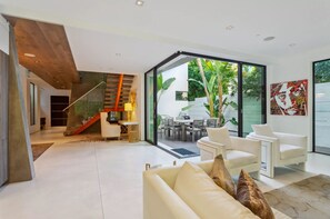 Una sala de estar moderna con un sofá blanco, un comedor con mesa y sillas, y una escalera que sube a un nivel superior.