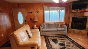 Een woonkamer met een beige leren bank, een beige zithoek, een houten vloer, een open haard en een televisie erboven.