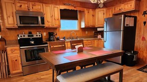 Een keuken met houten kastjes, roestvrijstalen apparatuur, een eettafel met roze placemats en een bank.