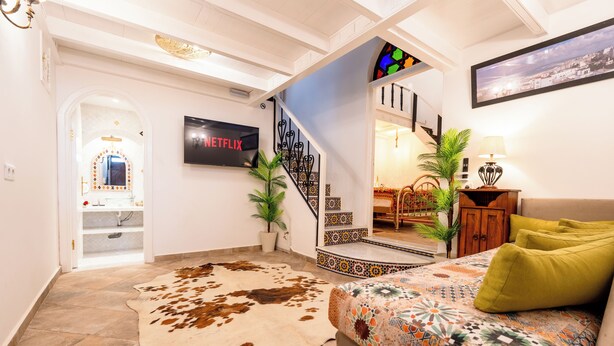A modern living room with a cowhide rug, a sofa with a colorful throw, a Netflix sign, a staircase with a stained glass window, and a view of the city through the window. - Kasbah Dream - Great Location in Tangier. (Tangier)