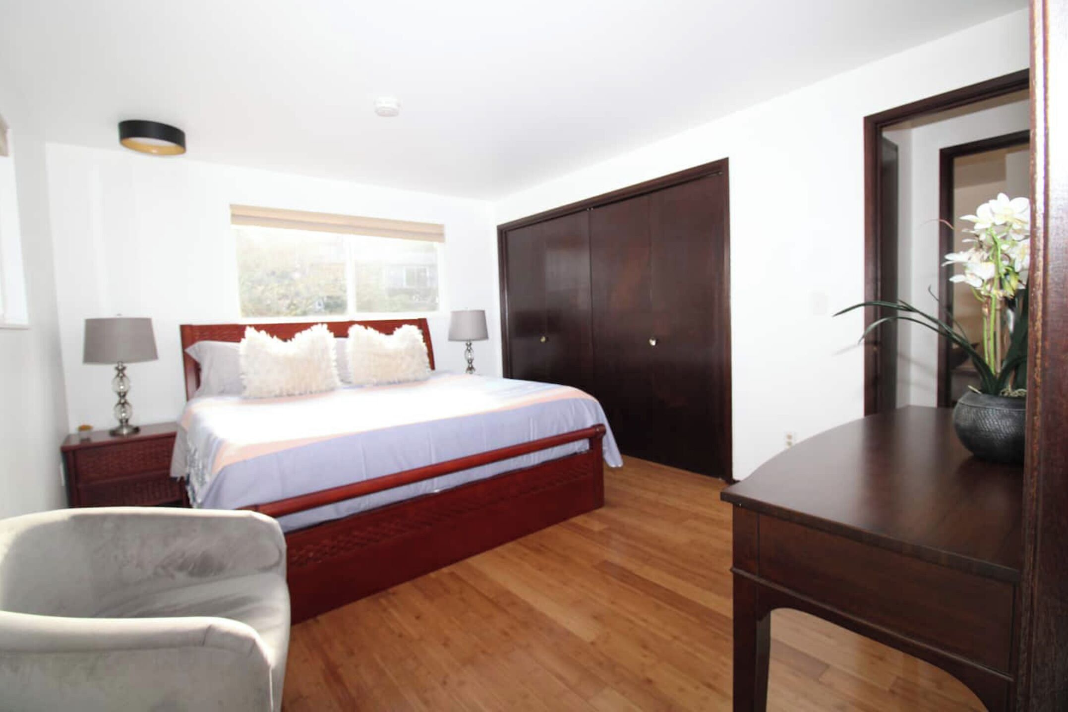Un dormitorio con cama de madera, mesita de noche, silla, escritorio, armario y ventana.