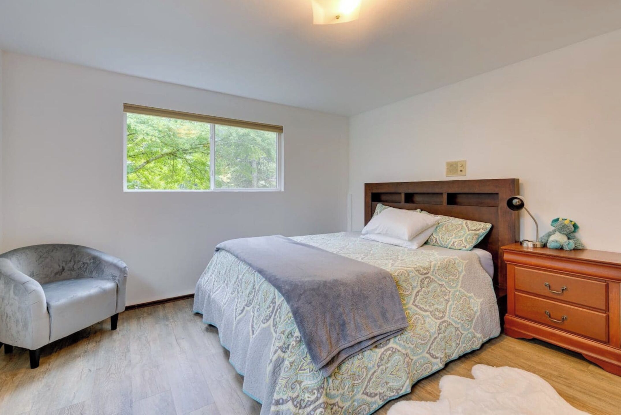 Une chambre à coucher avec un lit, une chaise, une table de chevet, une fenêtre et un plancher en bois.