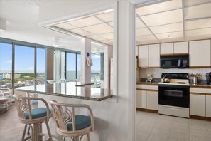A modern kitchen with a central island, white cabinetry, and a view of the ocean. - 2 Bedroom Condo with Ocean and Bay Views (Ocean City)