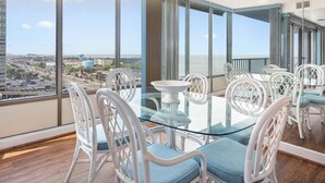 A balcony with a glass table and white wicker chairs, overlooking a cityscape. - 2 Bedroom Condo with Ocean and Bay Views (Ocean City)