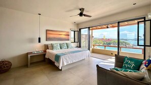 Ein Schlafzimmer mit Bett, Nachttisch, Sessel, Deckenventilator und einem großen Fenster mit Aussicht.