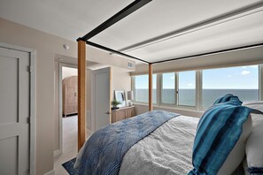 A bedroom with a large bed, a view of the sea through the window, and a door leading to another room. - Quay - Luxury Penthouse Condo! (Ocean City)