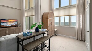 Una habitación con un ventanal grande, televisor, armario y una mesa con planta y pañuelos.