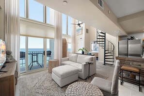 A spacious living area with a large window, a sofa, a coffee table, and a dining area with a wooden table and chairs.