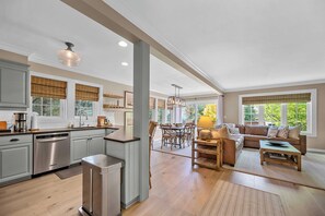 A spacious kitchen with modern appliances, a dining area with a wooden table and chairs, and a living room with a sofa and a lamp.
