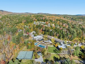 An aerial view of a residential area with houses, a tennis court, and a swimming pool surrounded by autumn-colored trees. - Stowe Drift: A luxurious 3-bedroom retreat at Top Notch Spa, perfect for families. (Stowe)