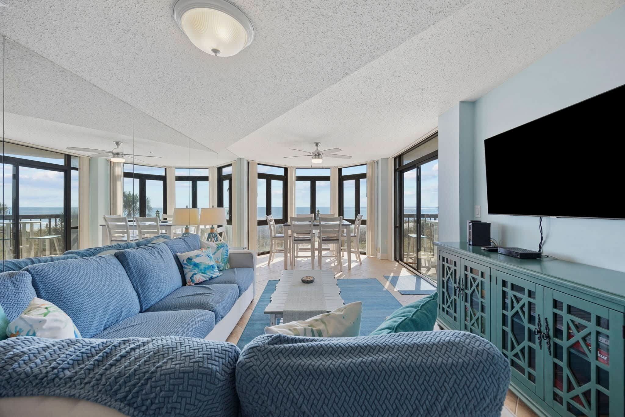 A spacious living area with a large sofa, a dining table, and a TV mounted on a cabinet.
