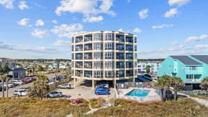 Ett hotell med flera våningar, ett poolområde, en parkeringsplats och omgivande byggnader.