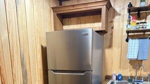 A stainless steel refrigerator in a kitchen with wooden walls and a wooden countertop. - 66 Tiny House (Clinton)