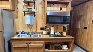 A compact kitchen with wooden cabinetry, a stainless steel sink, a microwave, and a variety of kitchen utensils and appliances. - 66 Tiny House (Clinton)