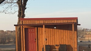 A small wooden structure with a red door, two chairs, and a table outside. - 66 Tiny House (Clinton)