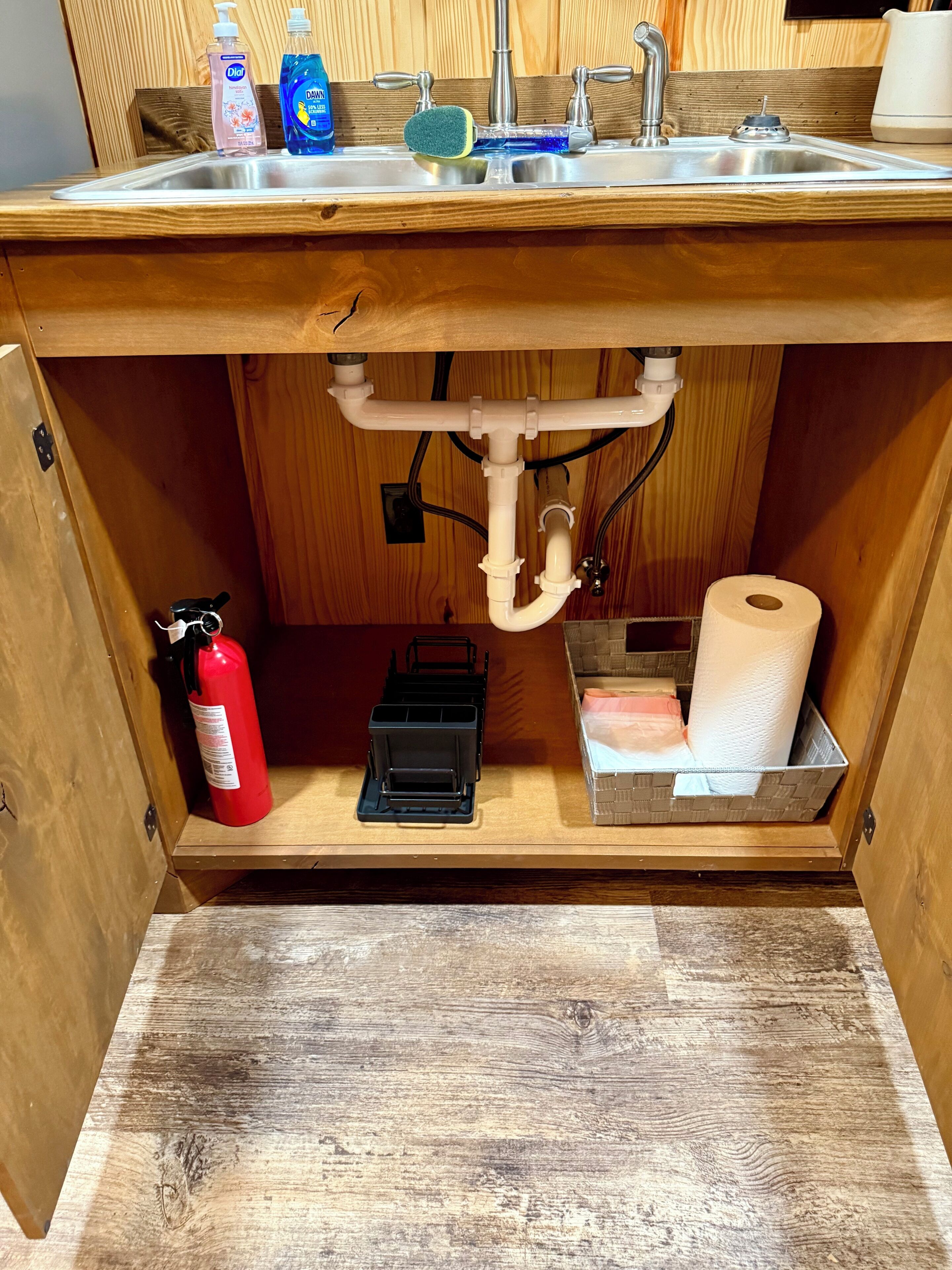A kitchen sink with cleaning supplies, a fire extinguisher, and a toilet paper holder.