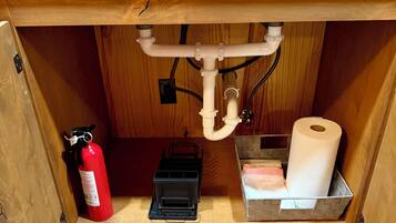 A kitchen sink with cleaning supplies, a fire extinguisher, and a toilet paper holder.