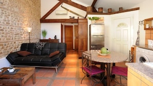 A cozy living area with a black leather sofa, a stone wall, and a kitchen with a stainless steel refrigerator and a washing machine. - GRENIER - PERPIGNAN - Gîte (PERPIGNAN)