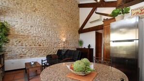 A kitchen with a stone wall, a round granite table, a black chair, and a stainless steel refrigerator. - GRENIER - PERPIGNAN - Gîte (PERPIGNAN)