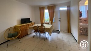 A small, clean room with a dining table, chairs, a television, and a chair with a cushion. - Le coscollet 1 - ILLE-SUR-TET (ILLE-SUR-TET)